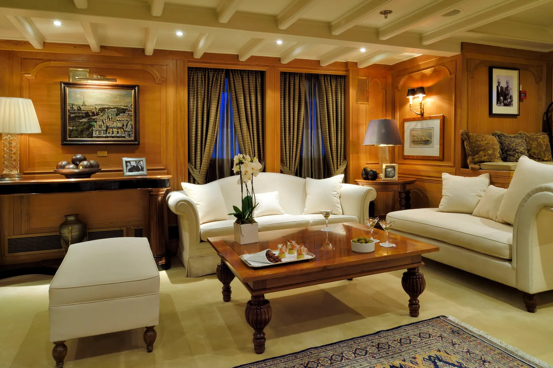 Timber-panelled main salon aboard CHRISTINA O with pale sofas and framed photographs