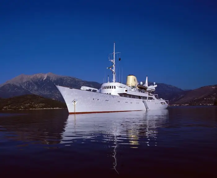 CHRISTINA O at anchor in still water below Greek mountains