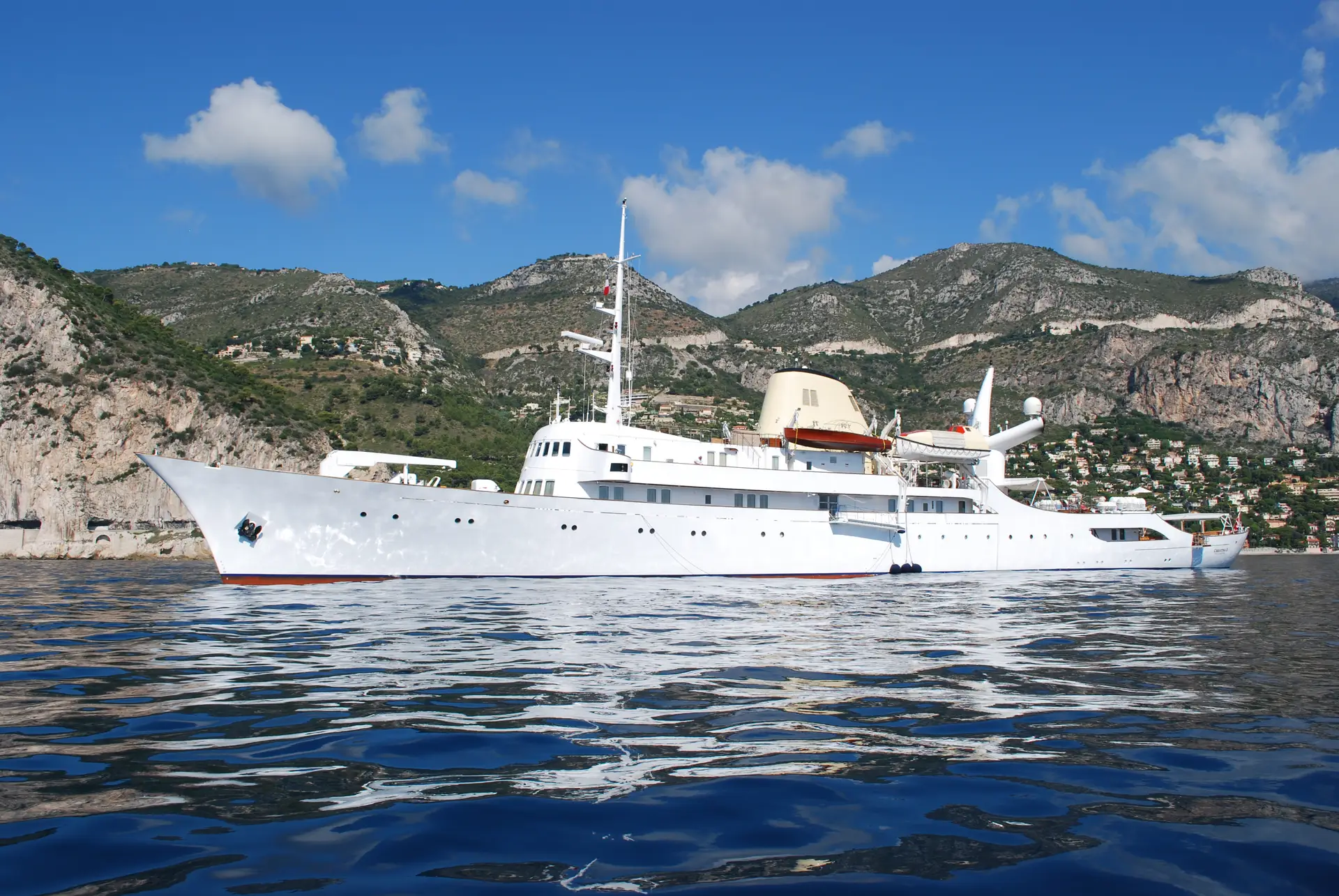 White hull of CHRISTINA O at anchor below the Riviera hills