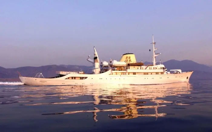 CHRISTINA O under way at dusk, mirrored in still water below distant hills